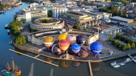 Hot air balloons inflate and tether from Bristol Harbourside as the countdown begins to the 2023 Bristol International Balloon Fiesta at Ashton Court Estate in August.