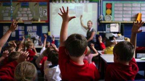 pupils with hands raised in a classroom