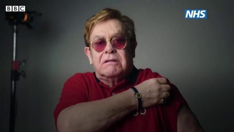 Elton John lifts up his sleeve to receive the vaccine.