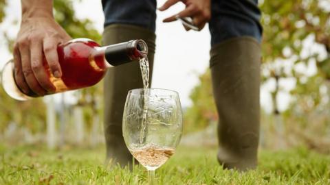 A man in wellies pouring a glass of wine