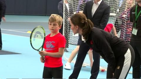 Duchess of Cambridge speaks to a boy holding a tennis racket