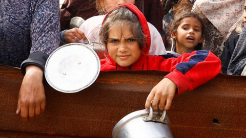 Displaced Palestinian children wait to receive free food at a tent camp