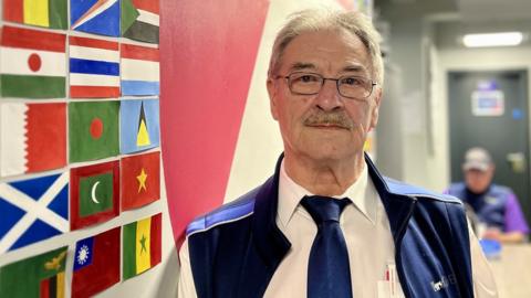 Douglas Hunt in front of painted flags at a First Bus Bristol depot