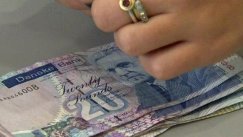 A bank cashier counts a small pile of £20 notes