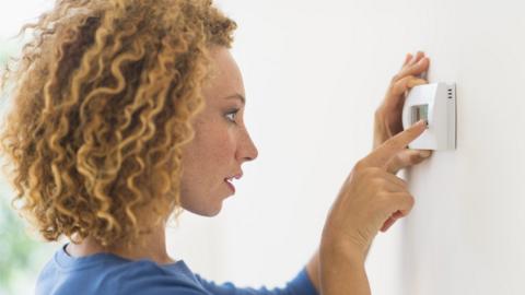 A woman operates a thermostat on the interior wall of a house