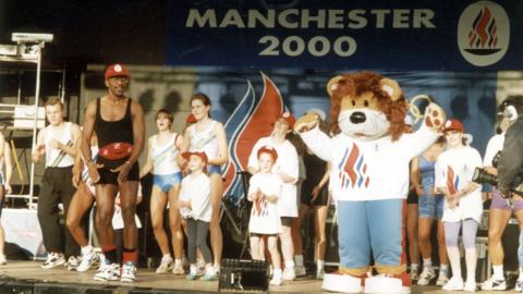 Mr Motivator, a mascot and some children on stage at an event in Manchester on the day in 1993 the 2000 Olympics host city was announced
