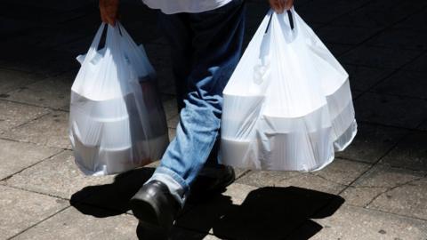 Takeaway food in containers being carried in white plastic carrier bags