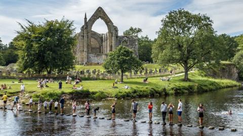 Bolton Priory overlooks the River Wharfe as families cross on stepping stones