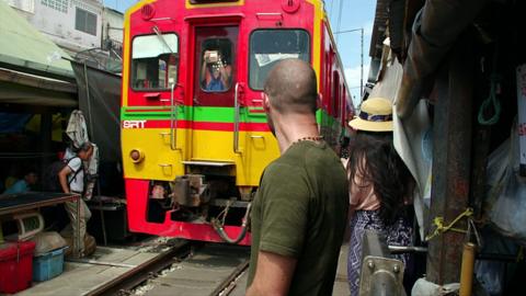 People watch a train move through Maeklong Station market