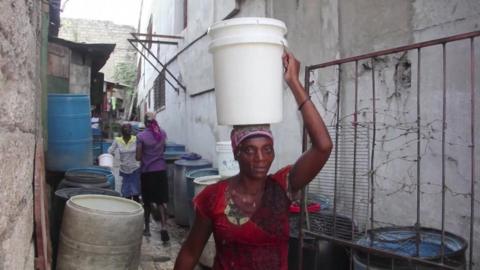 A woman carries a bucket of water on her head in Haiti