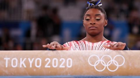 Simone Biles with her hands on a beam reading 'Tokyo 2020'