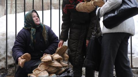 A 2010 file photo shows an elderly street vendor sitting in snowy weather while two passing pedestrians examine her woven straw shoes