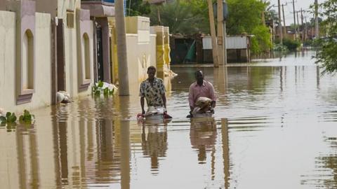 Two men wade through the floodwaters at Umm Dawm district in Khartoum, Sudan