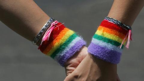 a lesbian couple wearing rainbow wristbands hold hands