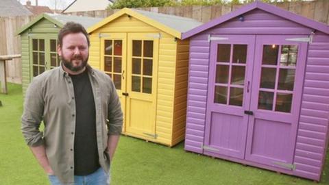 A man stands on a fake green next to a green, yellow, purple, pink and blue huts