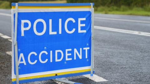 A blue and white "police accident" sign on an empty road.