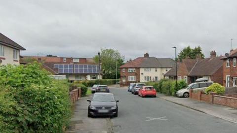 A street view image of the road shows a number of cars parked outside residential properties.