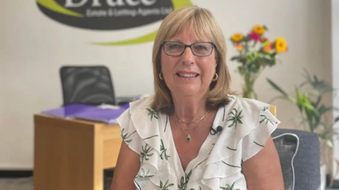 Linda Druce from Druce Estate & Letting Agents sitting in her office smiling into the camera 