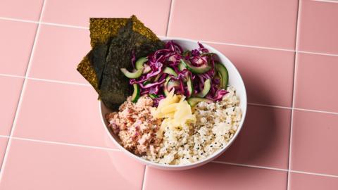 Rice, tuna and veg in a white bowl on a pink-tiled surface