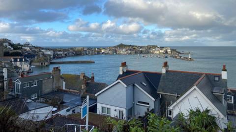 General view of St Ives in Cornwall. The image is taken from above a group of houses that overlook the sea on a sunny but cloudy day.