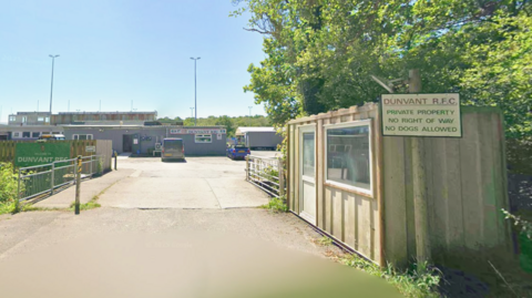 The entrance to Dunvant RFC. A clubhouse can be seen in the background with some cars parked and on the right, a sign says: Dunvant RFC. Private property no right of way. No dogs allowed.