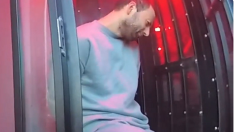 Klevi Pirjani, 37, who has short black hair and is wearing a grey sweatshirt and jogging bottoms, sits in the back of a police van with his hands behind his back.