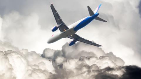 A plane flying through a grey cloudy sky.