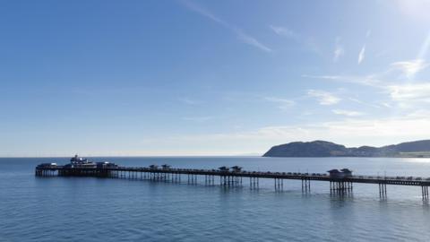 A pier stretching out to sea under a largely clear blue sky