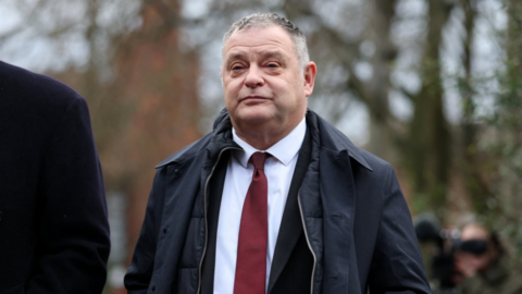 Mike Amesbury wearing a white shirt, red tie and dark overcoat