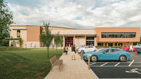 A computed-generated image of what the leisure centre at Five Acres will look like. It is a large, rectangular, modern building with a mix of stone and cladding on the exterior, with large windows revealing a gym where people are exercising. There is paving leading from the car park to the front door, with lots of people heading in.
