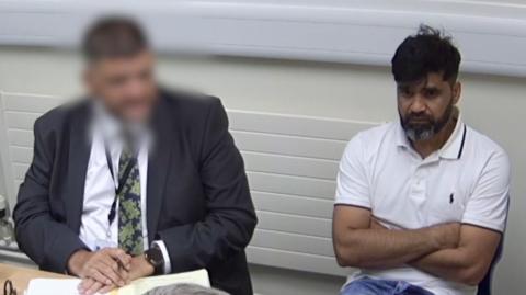 Urfan Sharif sat next to a translator, whose face is blurred