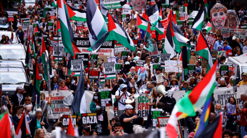 Protesters hold placards and wave Palestinian flags as they take part in a "National March for Gaza" in central London in 2024