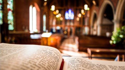 Religious book open in foreground with church pews in the background