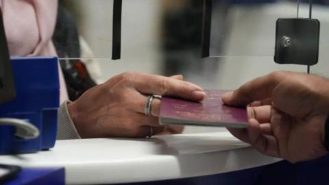 Someone passes over an old maroon Manx passport to passport control.