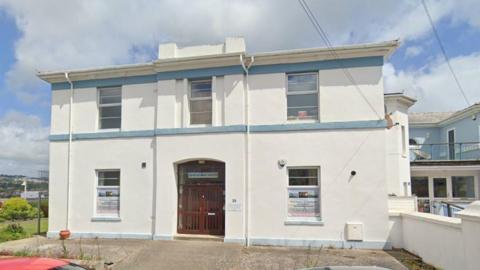 The anglers building which is being sold, it has a front door and is painted white with five windows.