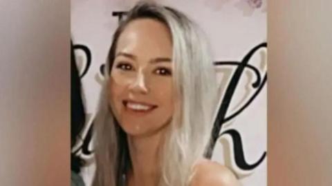 Sophie Evans in front of a white wall with stylised black writing. she is smiling and long blonde hair and brown eyes.