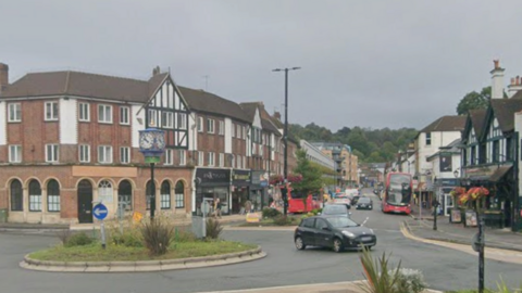 A road with a roundabout in the middle. Shop line the road coming off it.