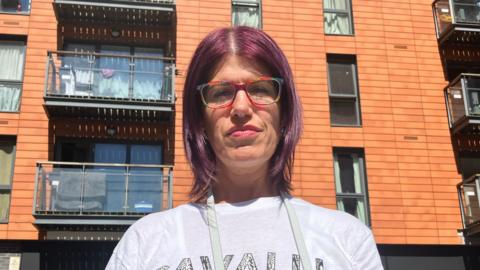 A picture of Fay Brooks-Hedges, who is stood in front of the block. Its cladding is visible on the walls behind her.