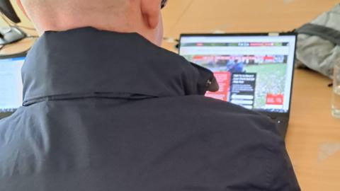 An over the shoulder rear view of a man wearing a black puffer coat looking at a laptop screen