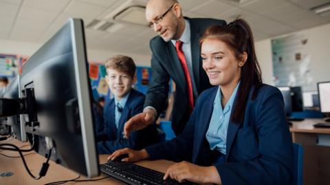 GCSE students and their teacher in a computer lab at school, discussing a project.