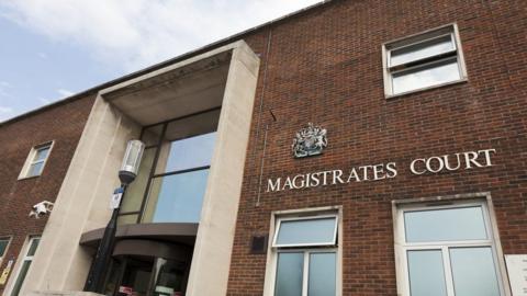 A close-up of the front of Portsmouth Magistrates' Court, looking up towards the sky. White letters spelling out "Magistrates Court" are mounted on the brick building, although the 'e' is slightly awry.