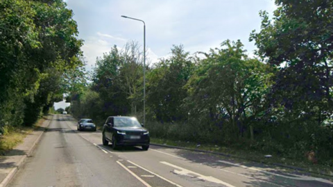 A long road surrounded by trees with cars driving on it