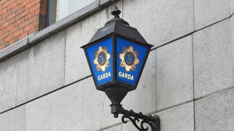 A Garda lamp. It is blue and black and attached to a wall.