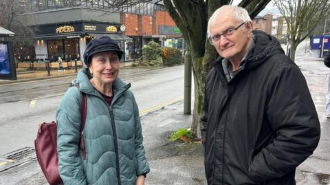 A man and woman stood next to each other in a street.