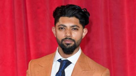 Qasim Akhtar in a suit standing in front of a red curtain