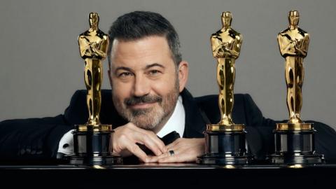 Jimmy Kimmel posing with Oscar statuettes