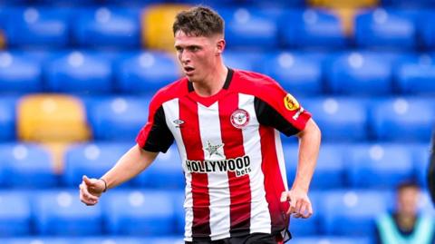 Fin Stevens running waist up shot waering Brentford red and white striped home kit
