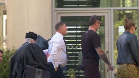 A group walking into Guernsey's Royal Court. In the centre is Jason Tardif, a man with black hair a grey beard wearing a white shirt and a navy blue tie. 