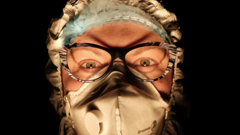 A female nurse wearing a face mask with a dark background behind her