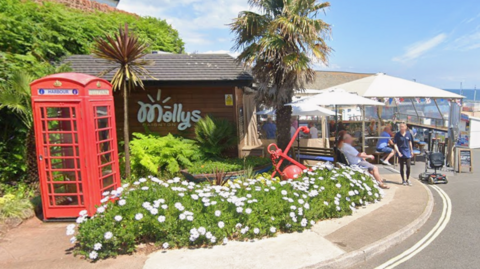 A picture taken from the outside looking at Mollys in Paignton. There is seating and tables under an umbrella to the right of the image.
